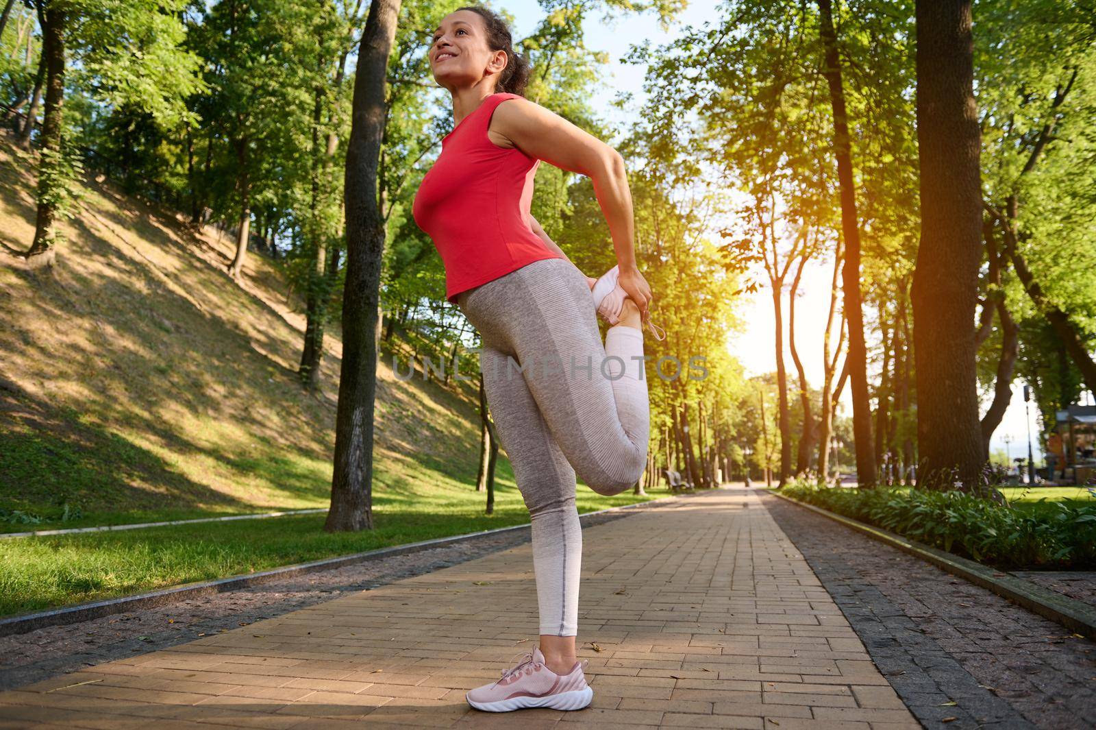 A sportswoman stretches her leg muscles during a morning workout in a city park. Sports and a healthy lifestyle to keep fit. Enjoy sport and keep your body fit by artgf