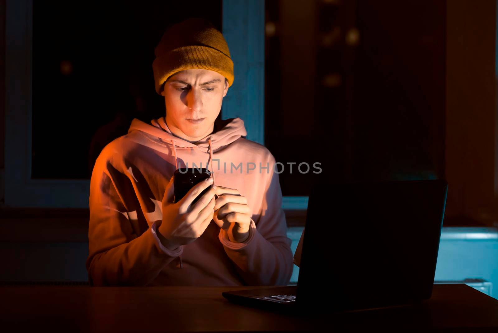 A young man works late at night at a laptop at home and talks on the phone, solves business issues, analyzes files, freelancer communicates online.