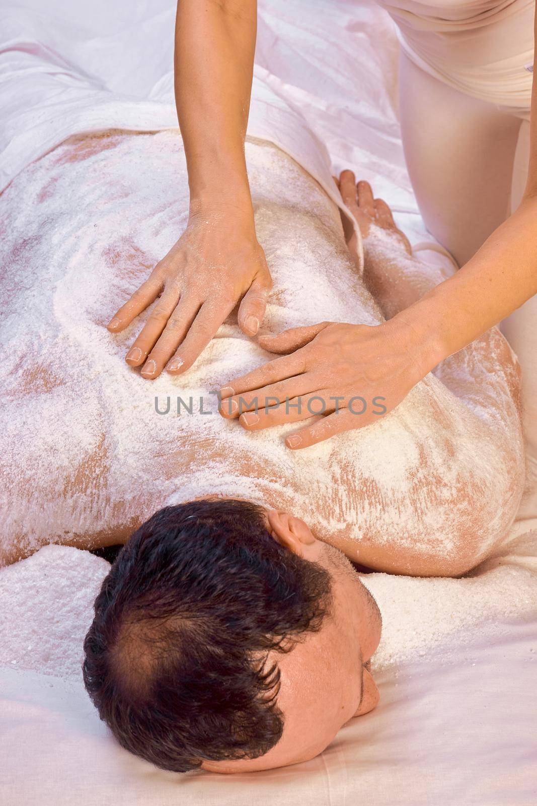 A woman healer performs a ritual with salt, rubs the back of a lying man with salt. Relaxation.