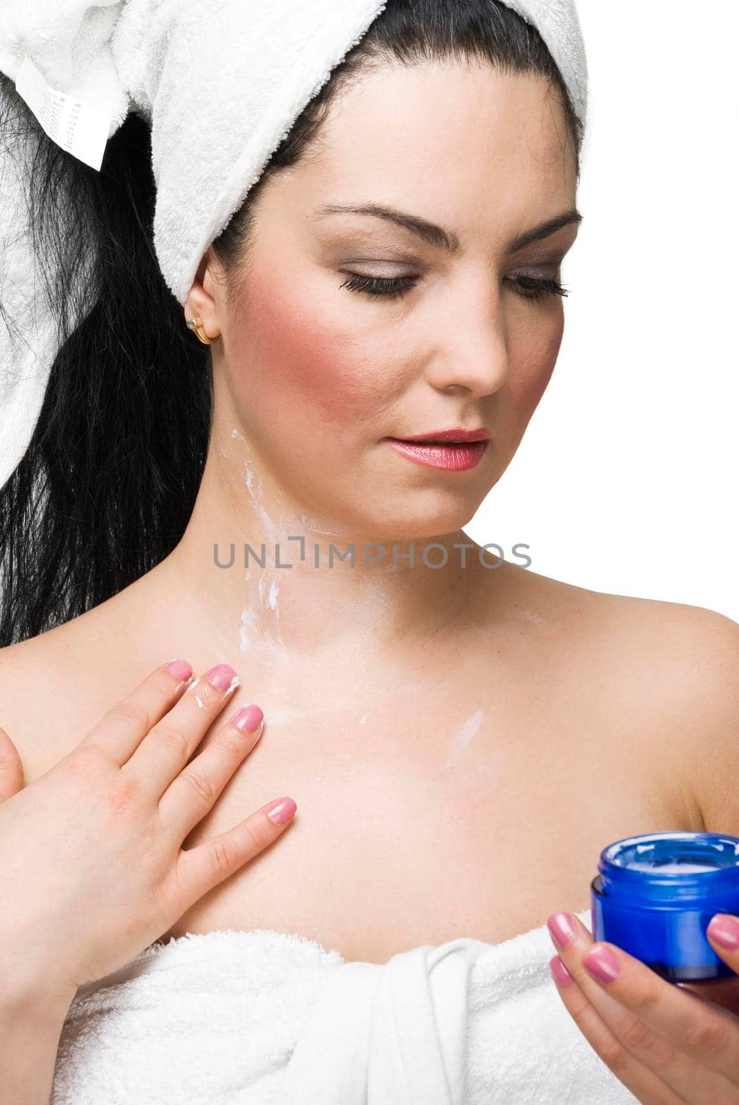 Portrait of beauty woman in white towel massaging her skin with cream ,holding a blue jar with cream and looking down isolated on white background
