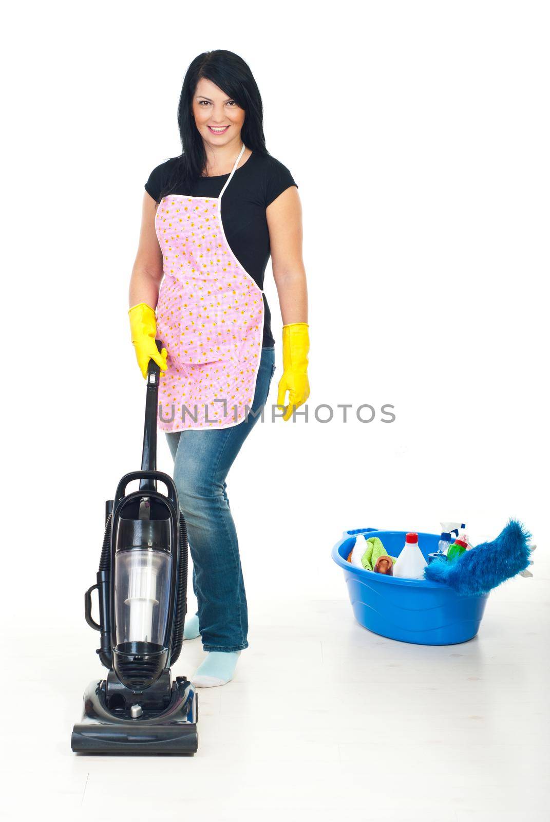 Cute brunette woman with pink apron using vacuum cleaner on floor in her home