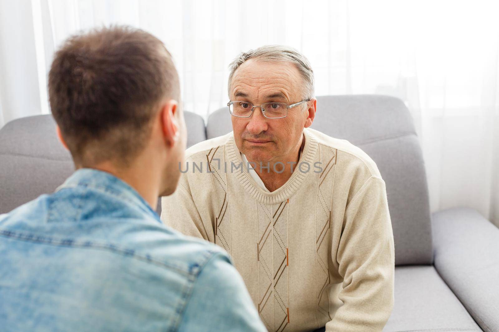 Young man sitting on a sofa smiling and talking with his grandfather