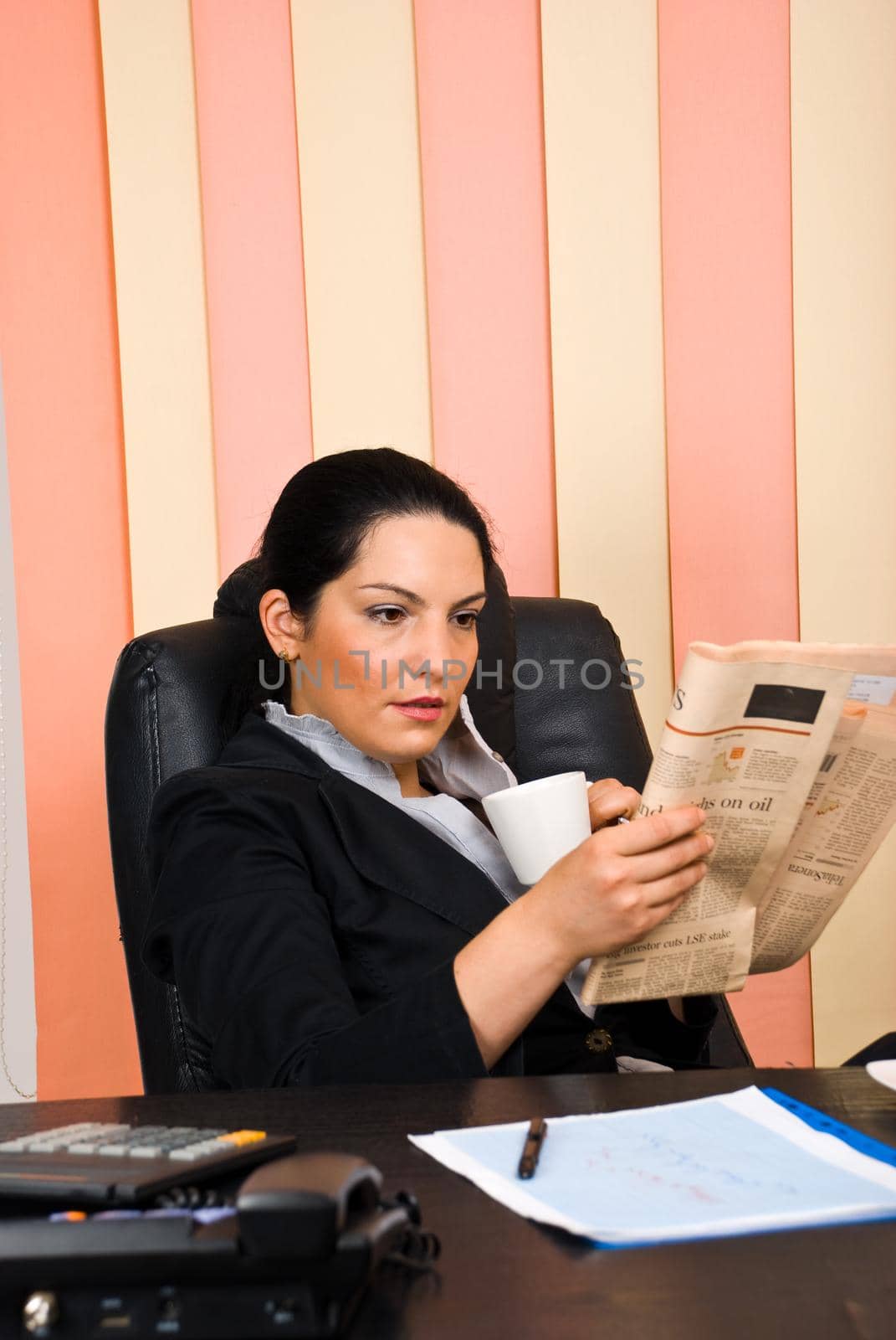 Young business woman sitting comfortable in her chair at office,drinking a cup of coffee and reading a newspaper