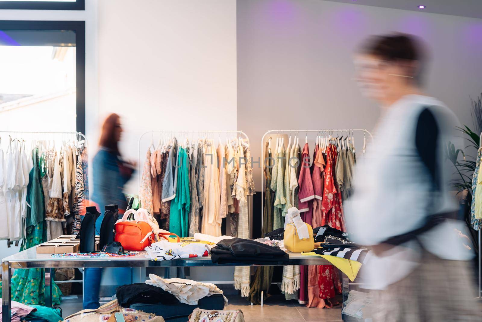 out of focus movement effect of two customers in a fashion shop. shopping concept. leisure concept. Natural light, sun rays, display, clothes rack, clothes, horizontal view, copying space.