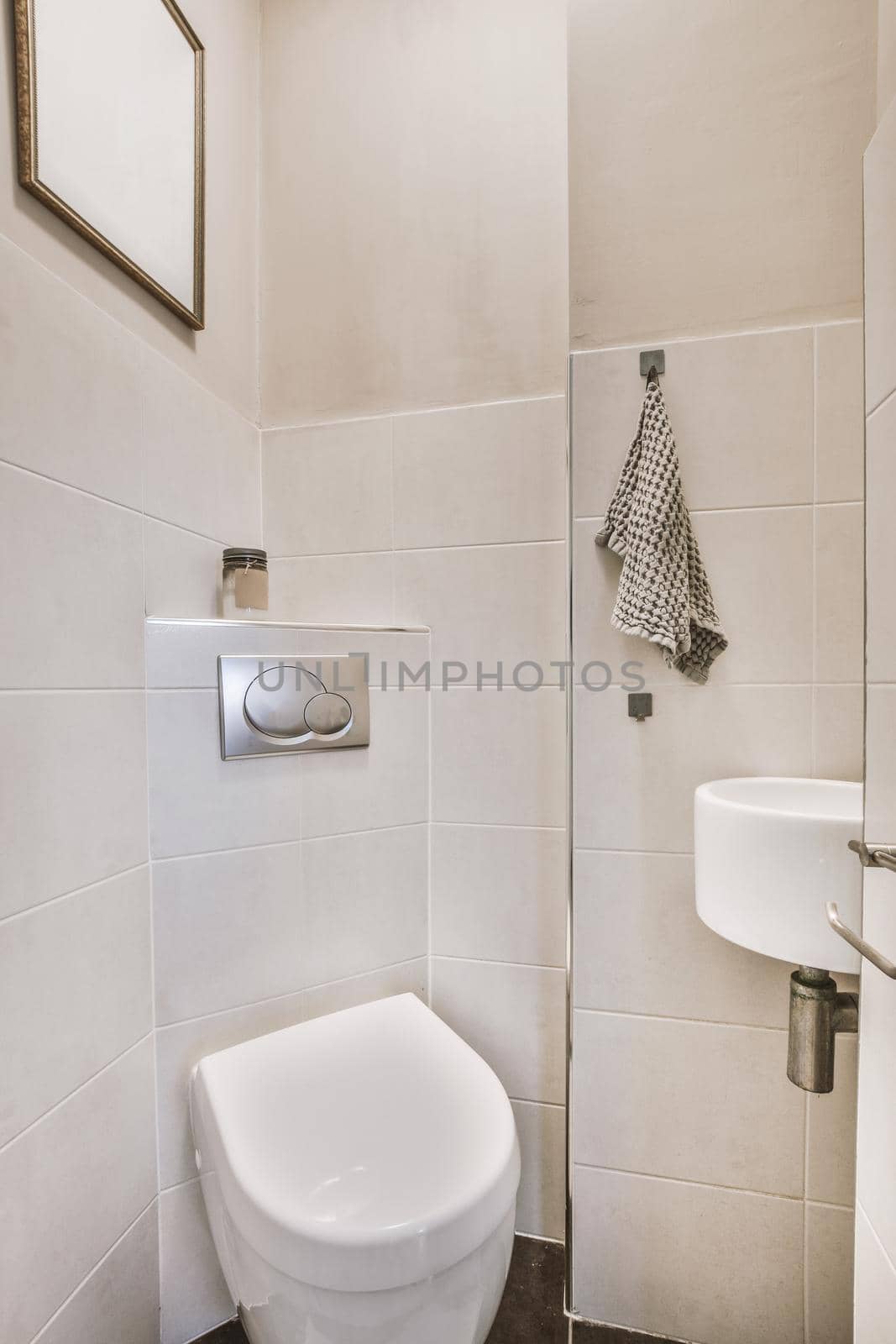 Interior of narrow restroom with sink and wall hung toilet with towel and checkered walls