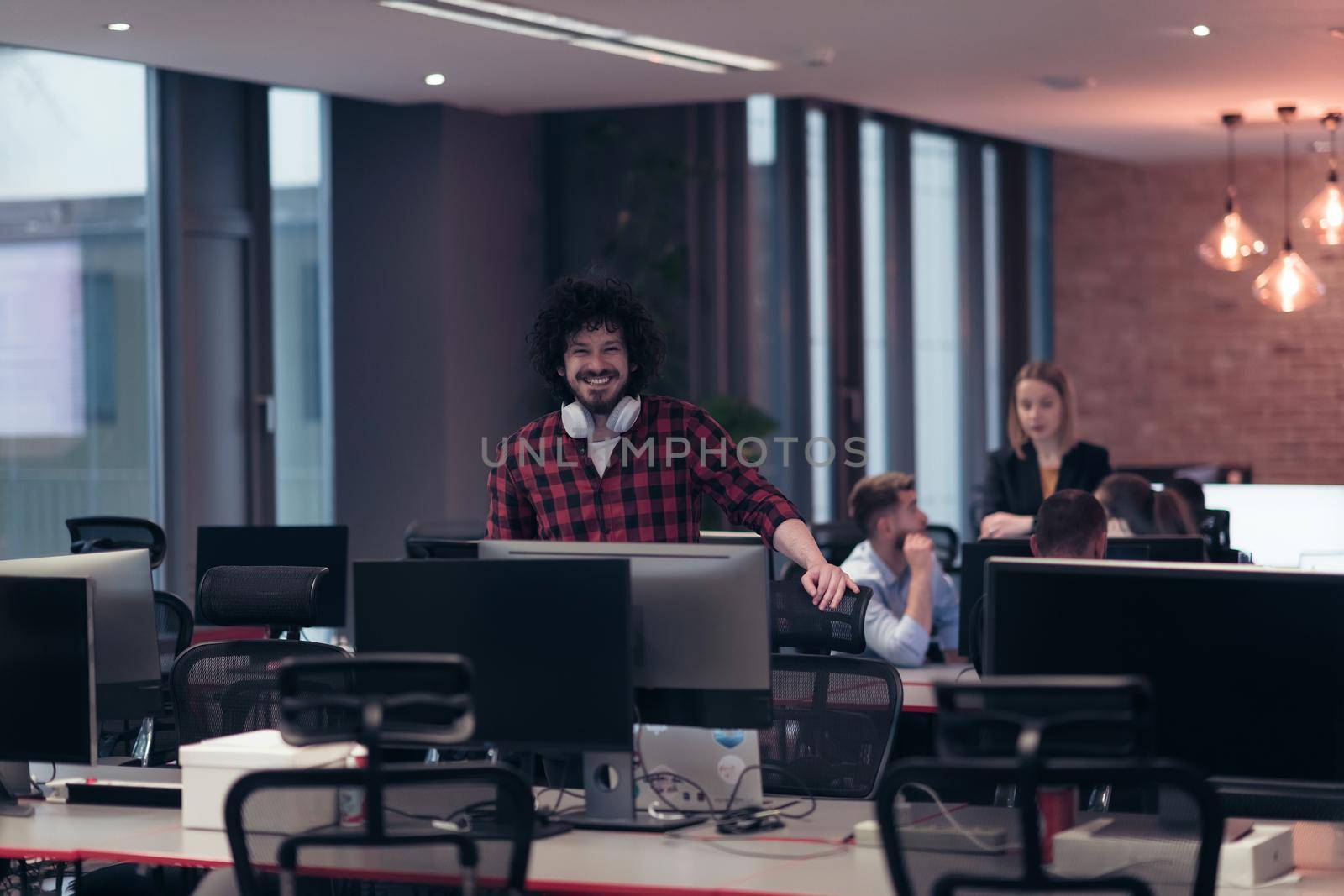 A young man with an Afro haircut stands in a modern office surrounded by computers. High-quality photo