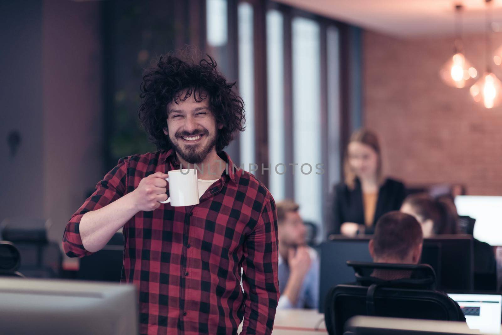 Smiling businessman in afro shirt standing in a modern office with a cup of coffee in hand. Selective focus. High-quality photo