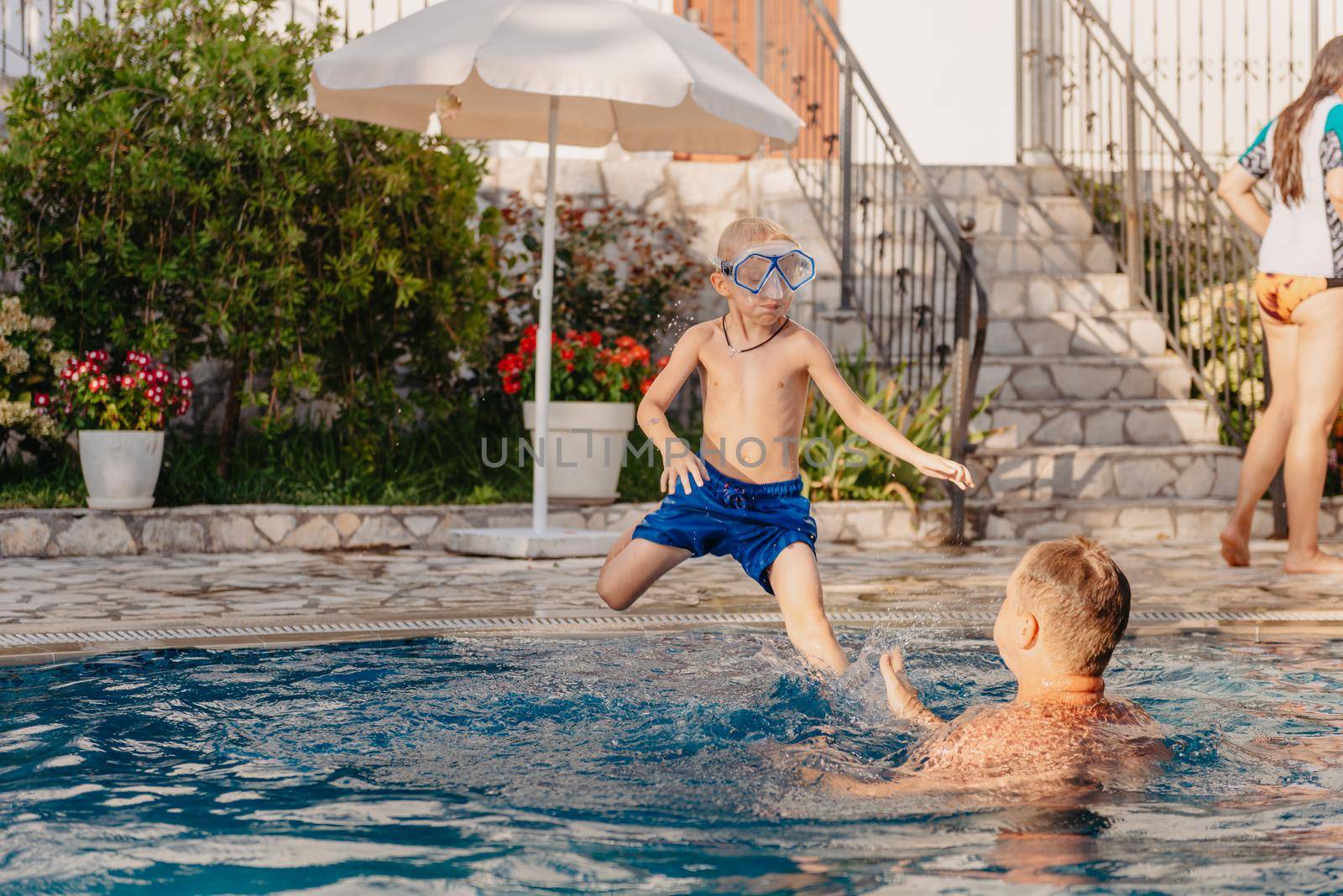 Excited boy in googles jumping in water from shoulders of his father standing in swimming pool by Andrii_Ko