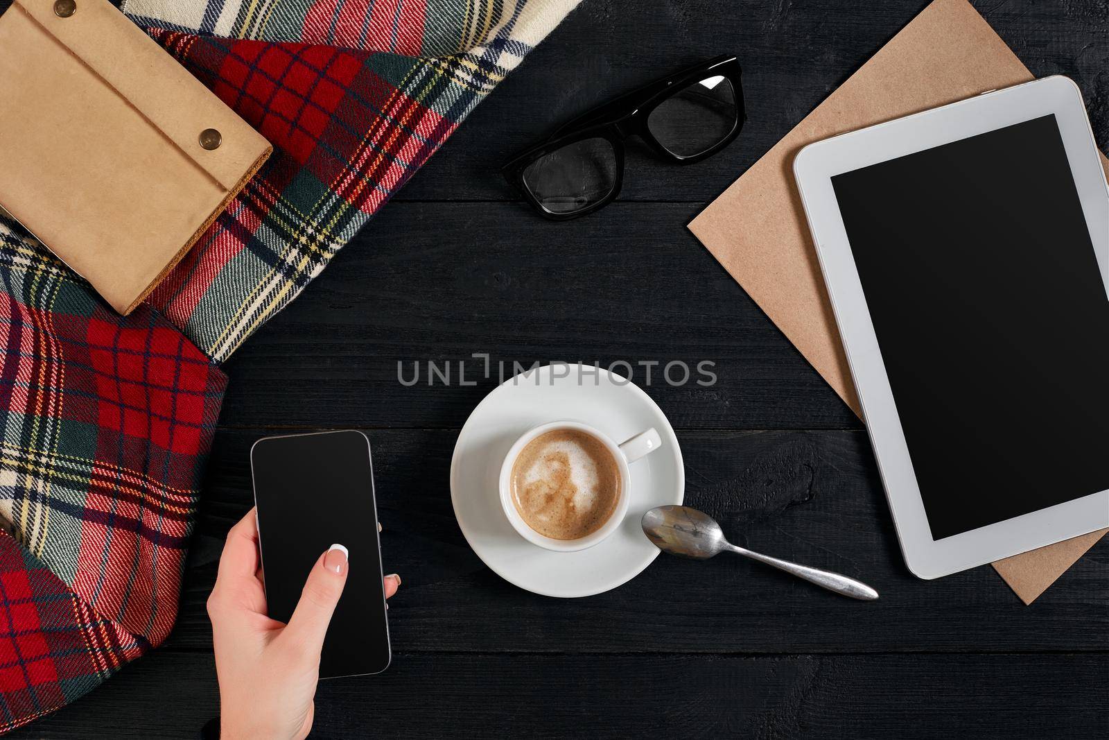 Women hands holding the phone with black screen above the table with a cup of coffee and tablet. Top view, flat lay. Copy space. Still life. Cafe.