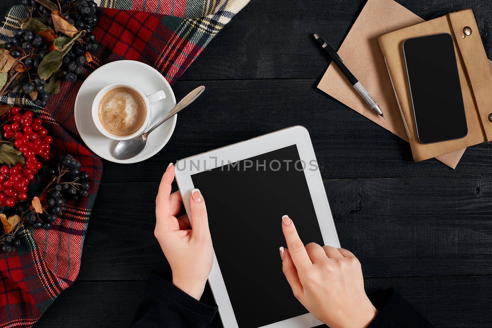 Women hands holding the tablet with black screen above the table with a cup of coffee and smart. Top view, flat lay. Copy space. Still life. Cafe.