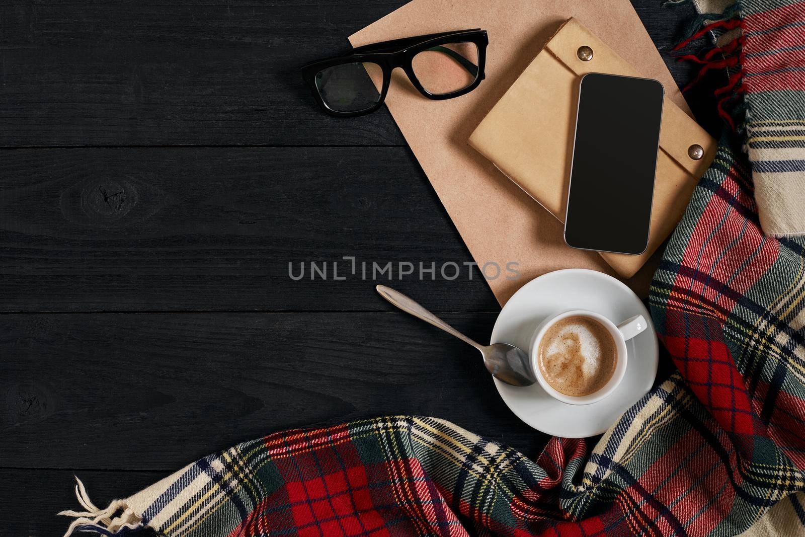 Above view of Smart phone with notebook and cup of latte coffee on black wooden background. Still life. Copy space. Flat lay. Top view