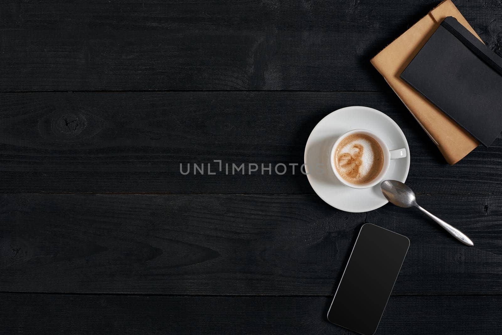 Smartphone with notebook and cup of coffee on wooden background. Top view. Copy space. Still life. Flat lay. Cafe.