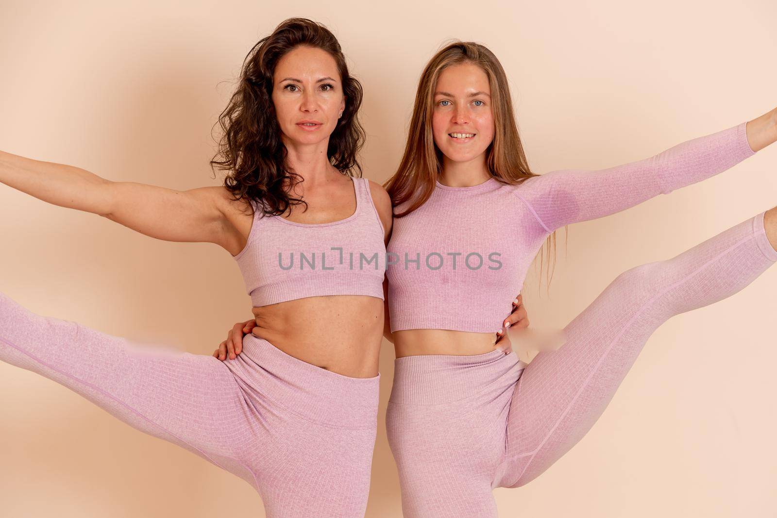 Two beautiful women cook doing yoga, sports together in the gym. Dressed in pink suits. The concept of grace and beauty of the body. by Matiunina