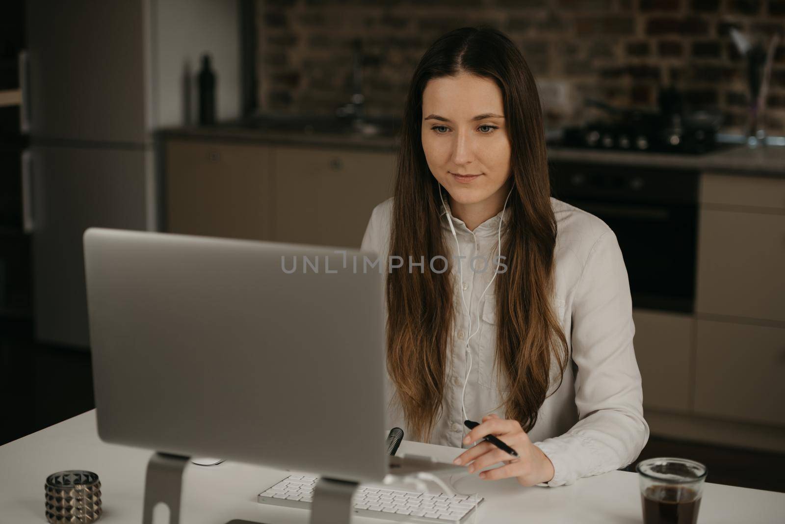 Remote work. A caucasian brunette woman with headphones working remotely on her laptop. A lady in a white shirt doing business at her home workplace.