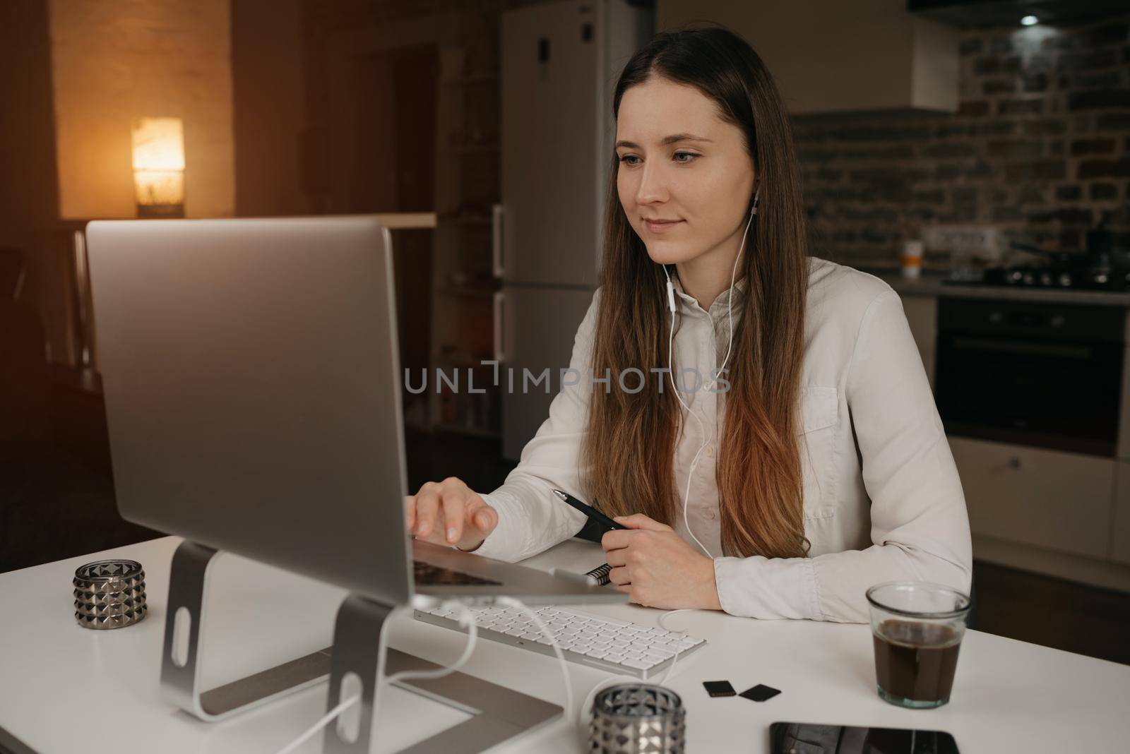 Distance learning. A caucasian woman with headphones studying remotely online on her laptop. A girl watching a webinar at her cozy home workplace.