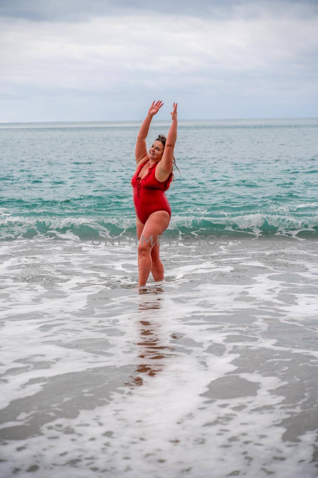 Woman in a bathing suit at the sea. A fat young woman in a red swimsuit enters the water during the surf by Matiunina