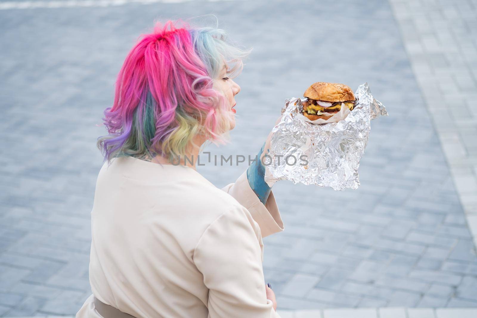 Caucasian woman with curly colored hair eating burger. Bad eating habits and love of fast food.