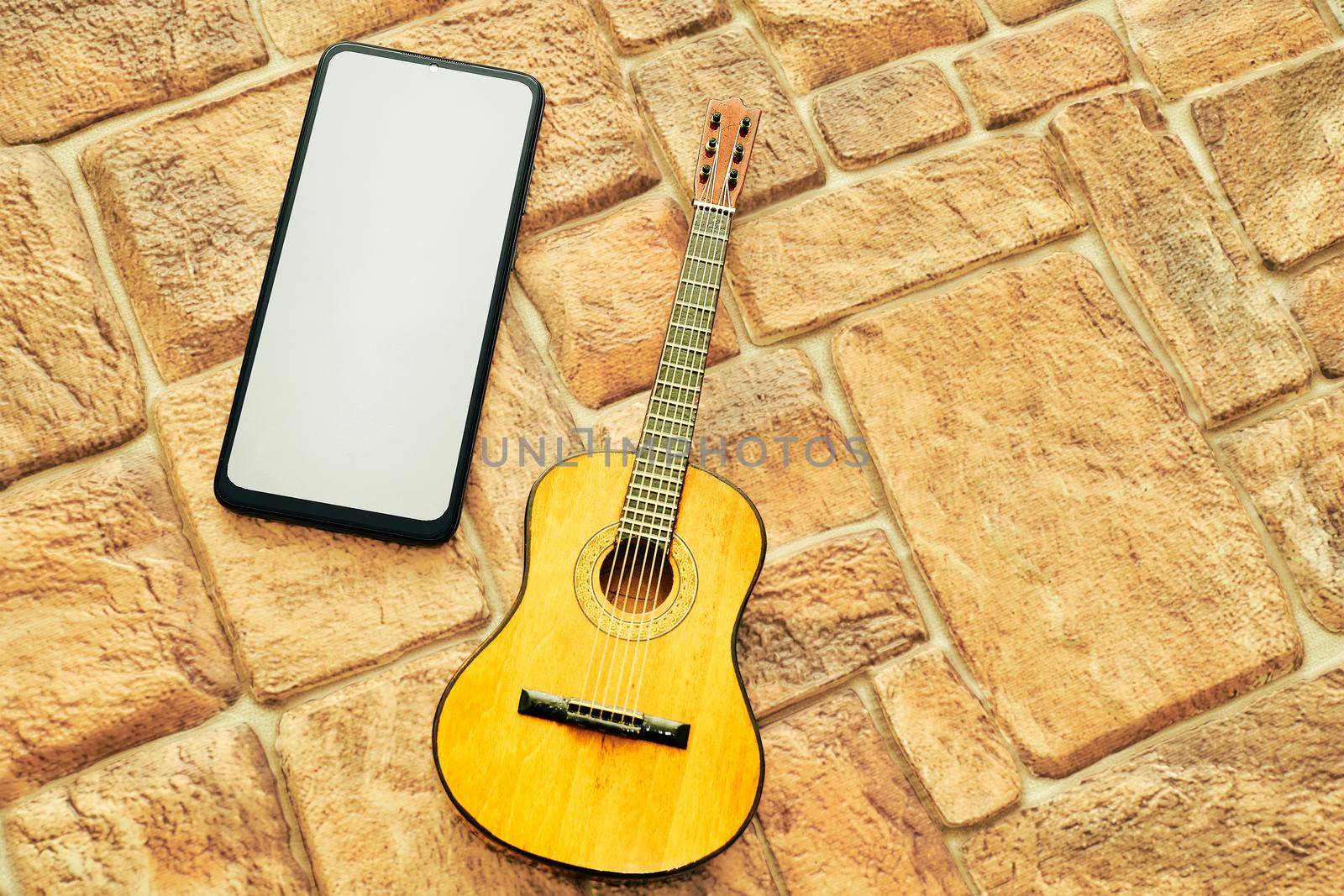 Phone with space for text, acoustic guitar on a cobbled yellow sand background by jovani68