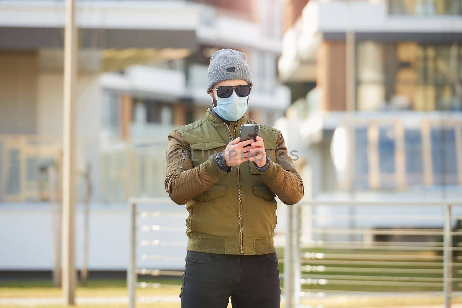A man in a medical face mask to avoid the spread coronavirus waiting in the cozy street. A fellow checking sunglasses wears a cap and a face mask against COVID 19.