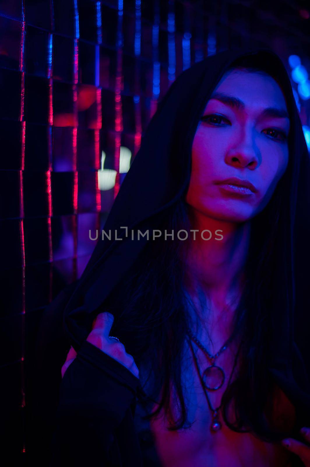 Close-up portrait of an androgenic model in a hood. Male transgender in studio with neon light
