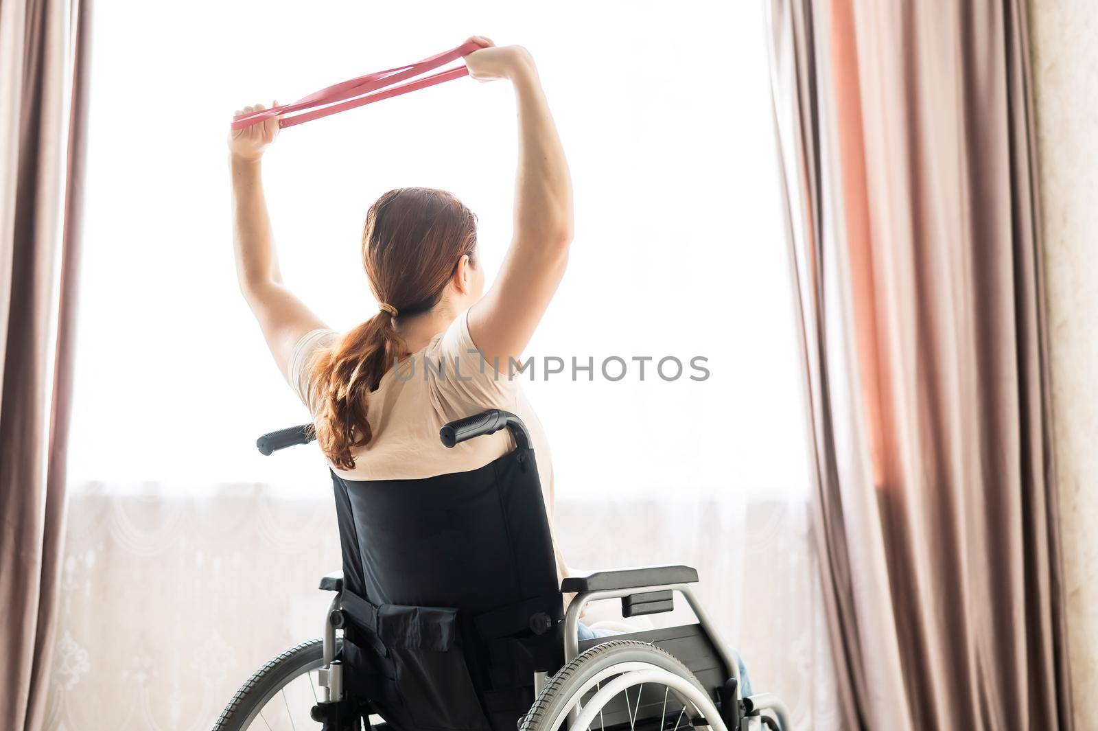 Caucasian woman in a wheelchair doing exercises with the help of fitness rubber bands. by mrwed54