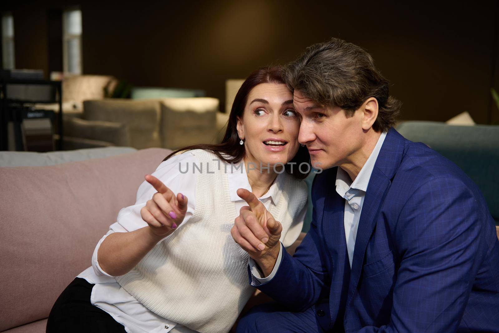 Charming middle-aged Caucasian married couple choosing for sofa in the upholstered furniture store. Home interior design, house improvement and renovation concept