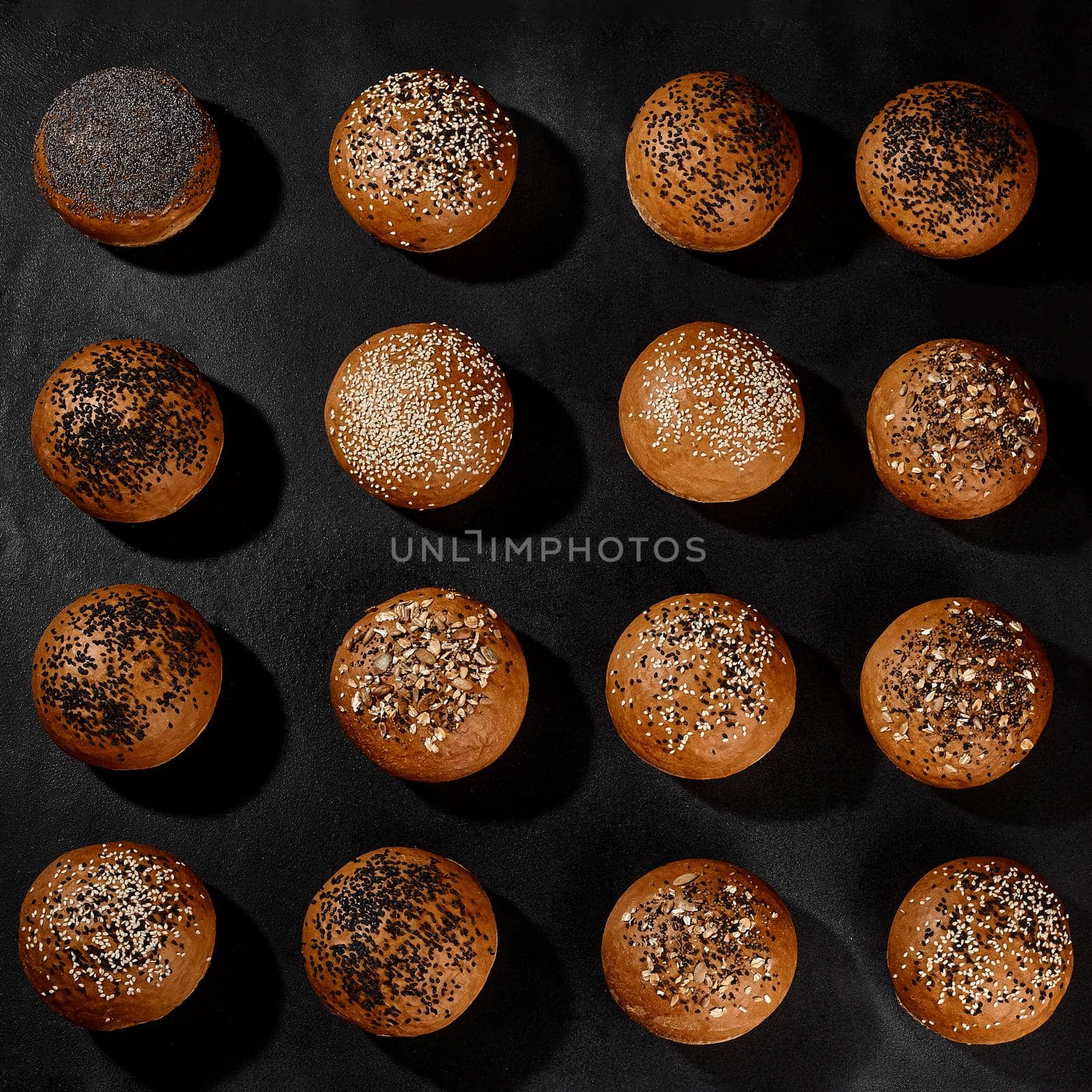 Variety of fresh, tasty baked buns with black and white sesame and sunflower seeds against black background with copy space. Close-up by nazarovsergey