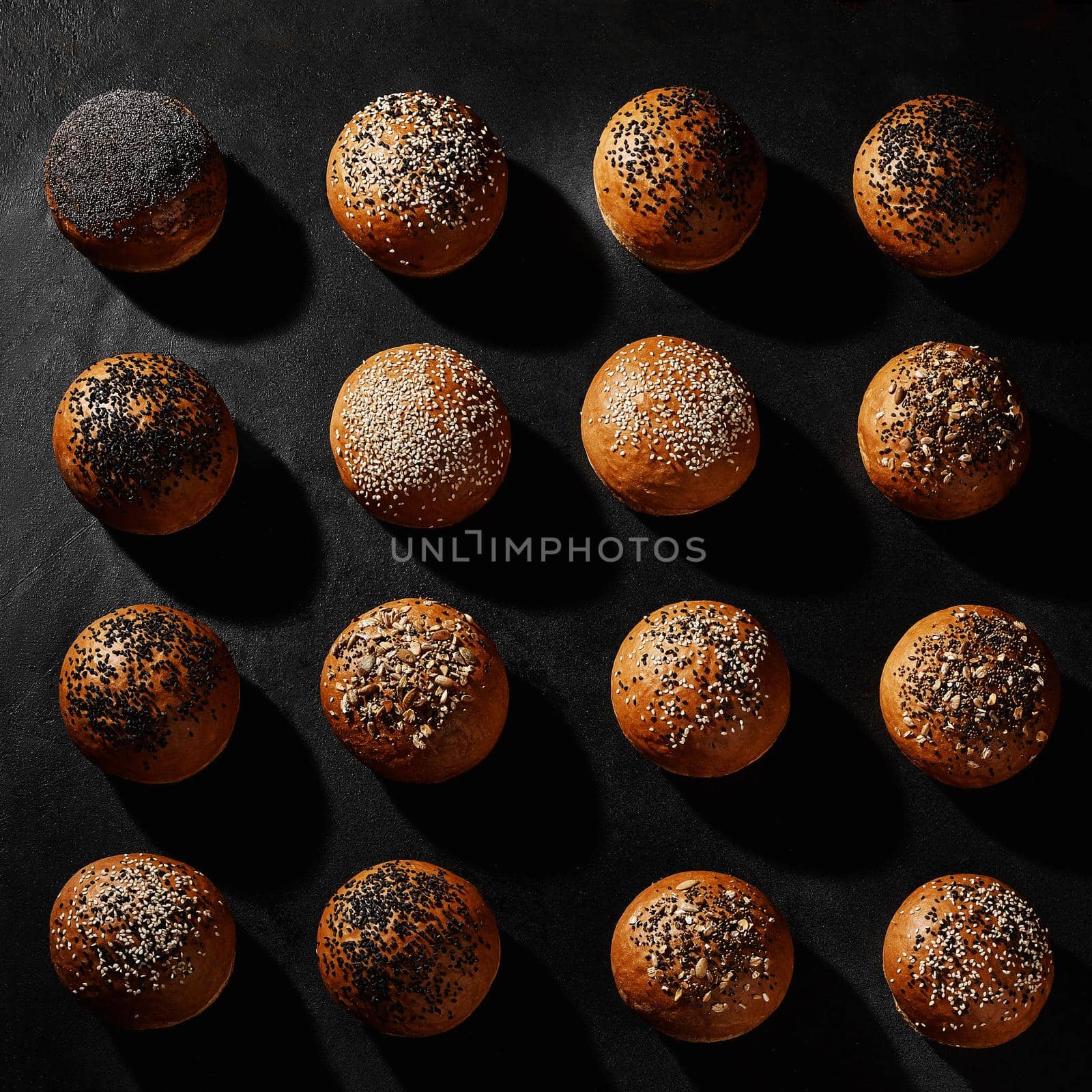 Assortment of fresh, delicious baked buns with black and white sesame and sunflower seeds against black background with copy space. Close-up by nazarovsergey