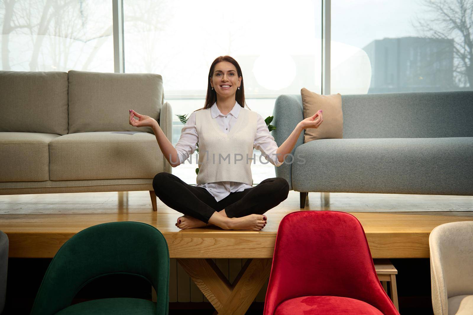 Peaceful relaxed middle-aged beautiful Caucasian woman seller in a furniture store, sits in a lotus position and meditates. The concept of tranquility and a client-oriented approach