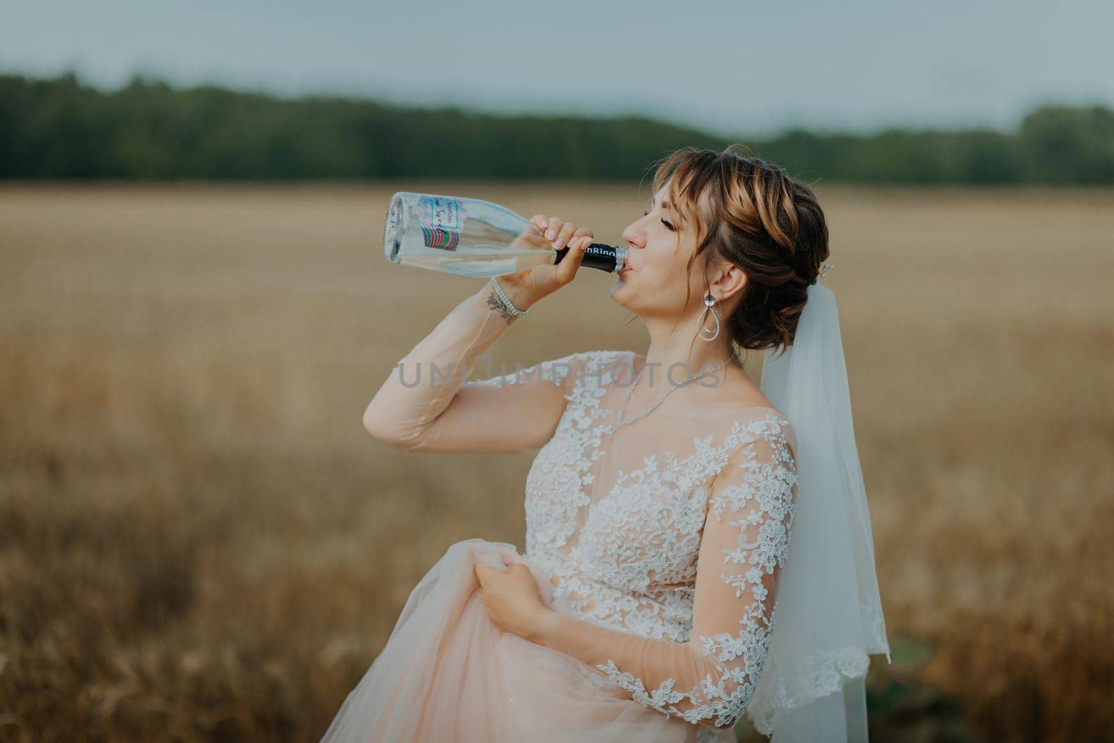 Girl in wedding dress and white veil drinking champagne from bottle