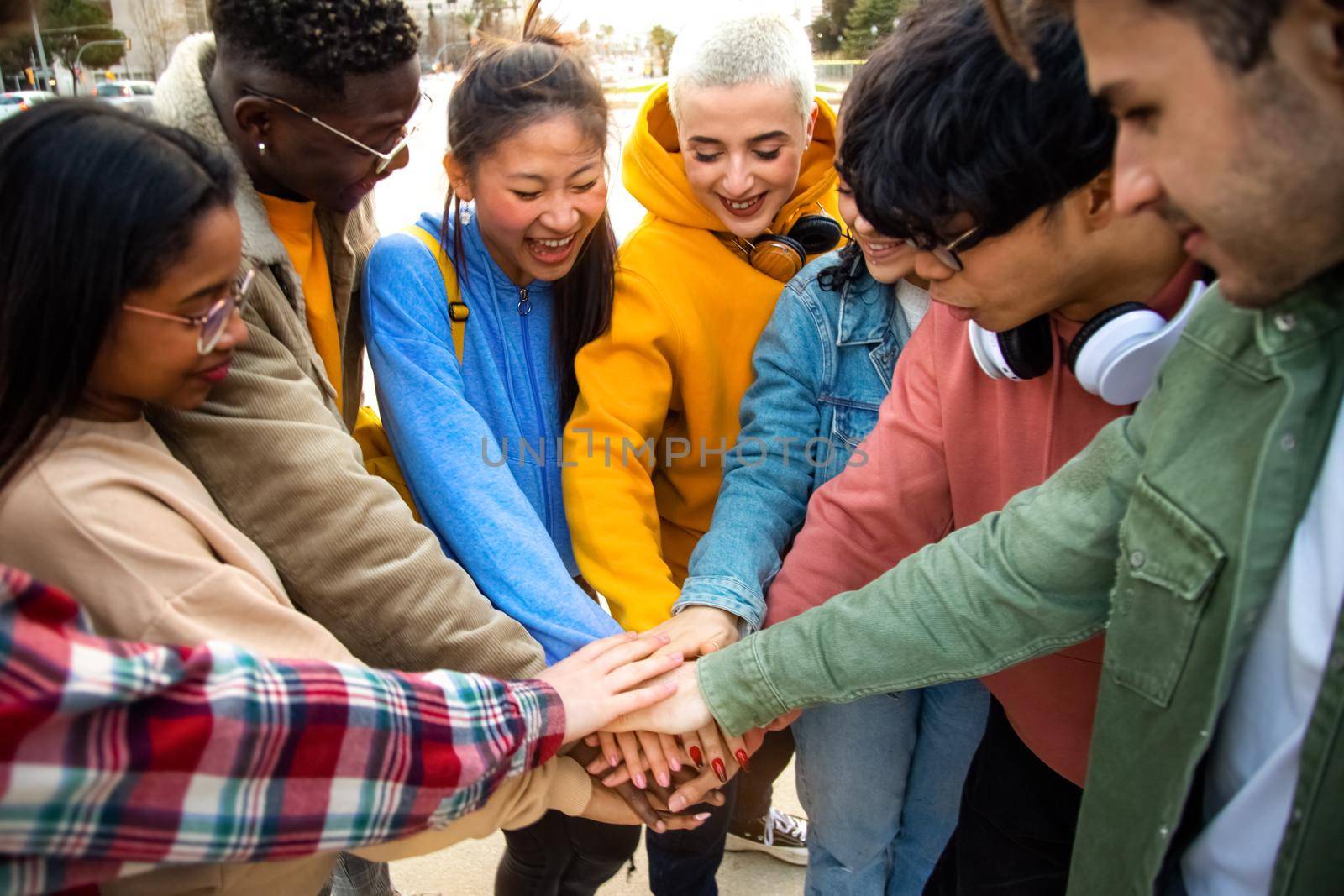 Group of multiracial college students stack hands together in a circle outdoors. by Hoverstock