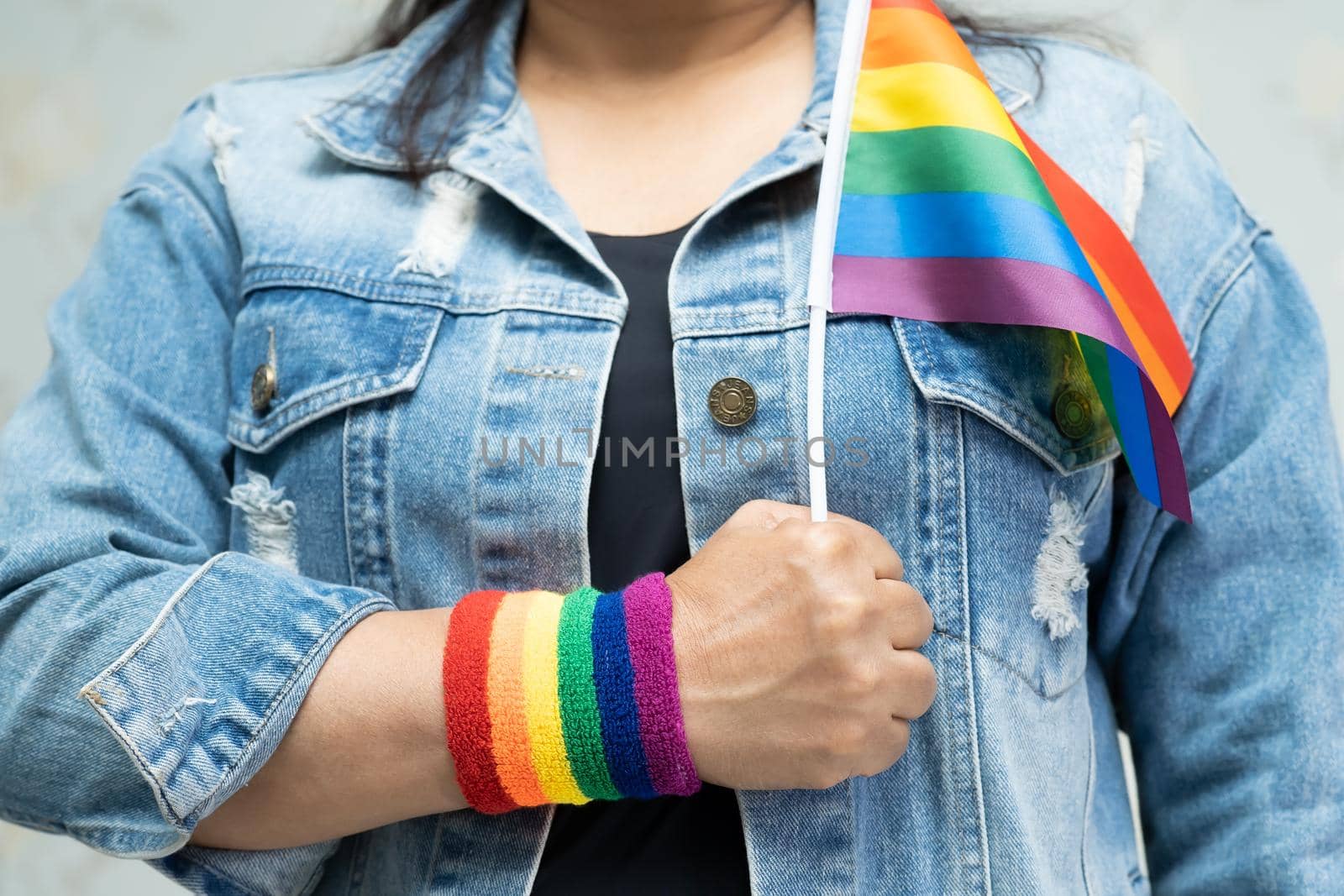 Asian lady wearing blue jean jacket or denim shirt and holding rainbow color flag, symbol of LGBT pride month celebrate annual in June social of gay, lesbian, gay, bisexual, transgender, human rights.