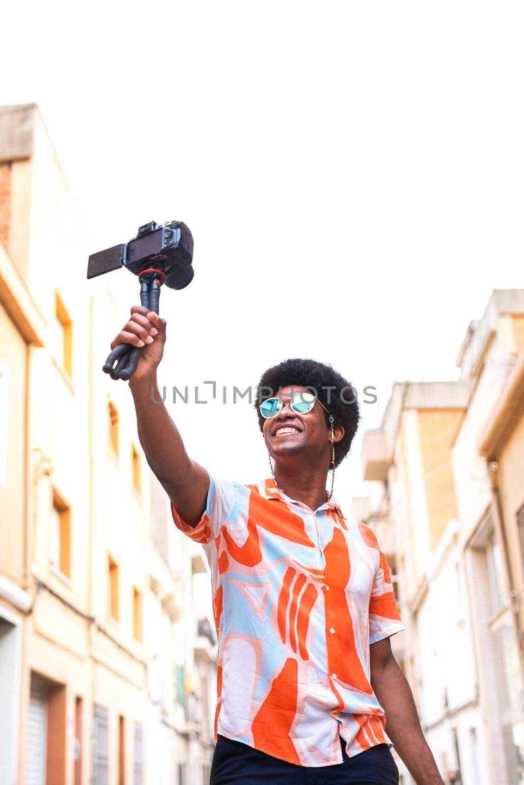 Young African American man vlogging his vacation trip for social media platform. Copy space. Vertical image. by Hoverstock