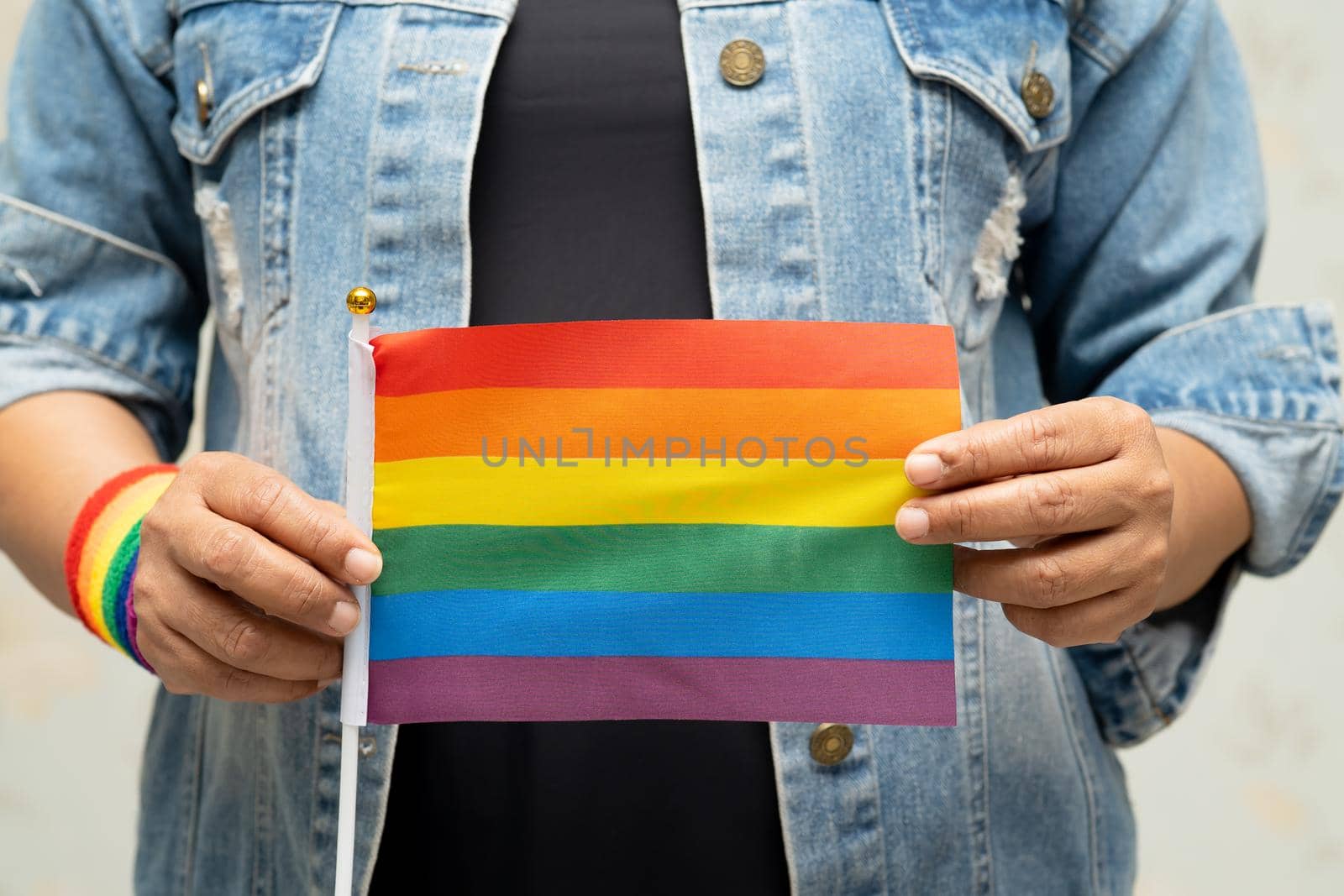 Asian lady wearing blue jean jacket or denim shirt and holding rainbow color flag, symbol of LGBT pride month celebrate annual in June social of gay, lesbian, bisexual, transgender, human rights.