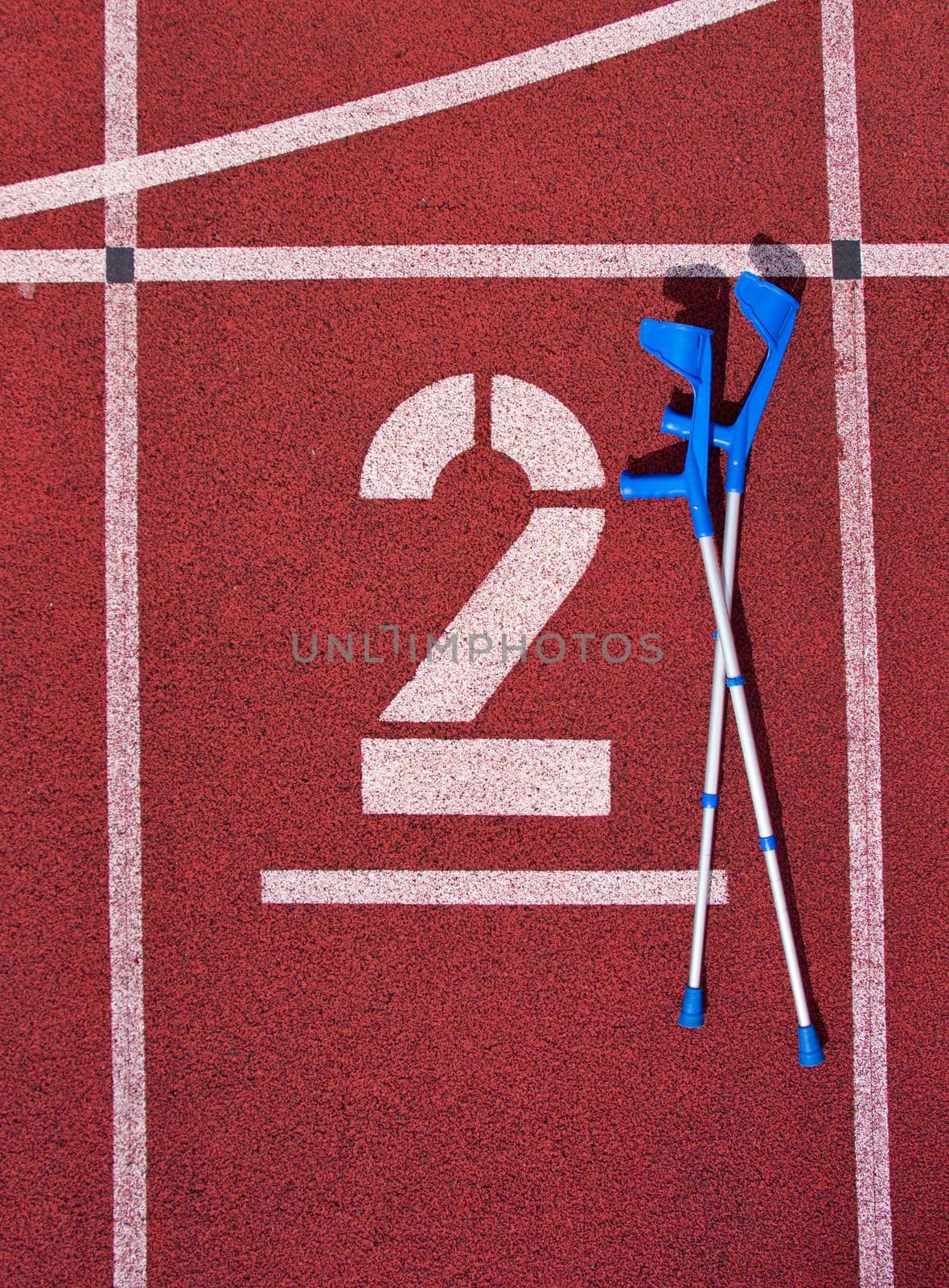 Medicine crutch at number two. Big white track number on red rubber racetrack. Gentle textured running racetracks in small outdoor stadium. by rdonar2