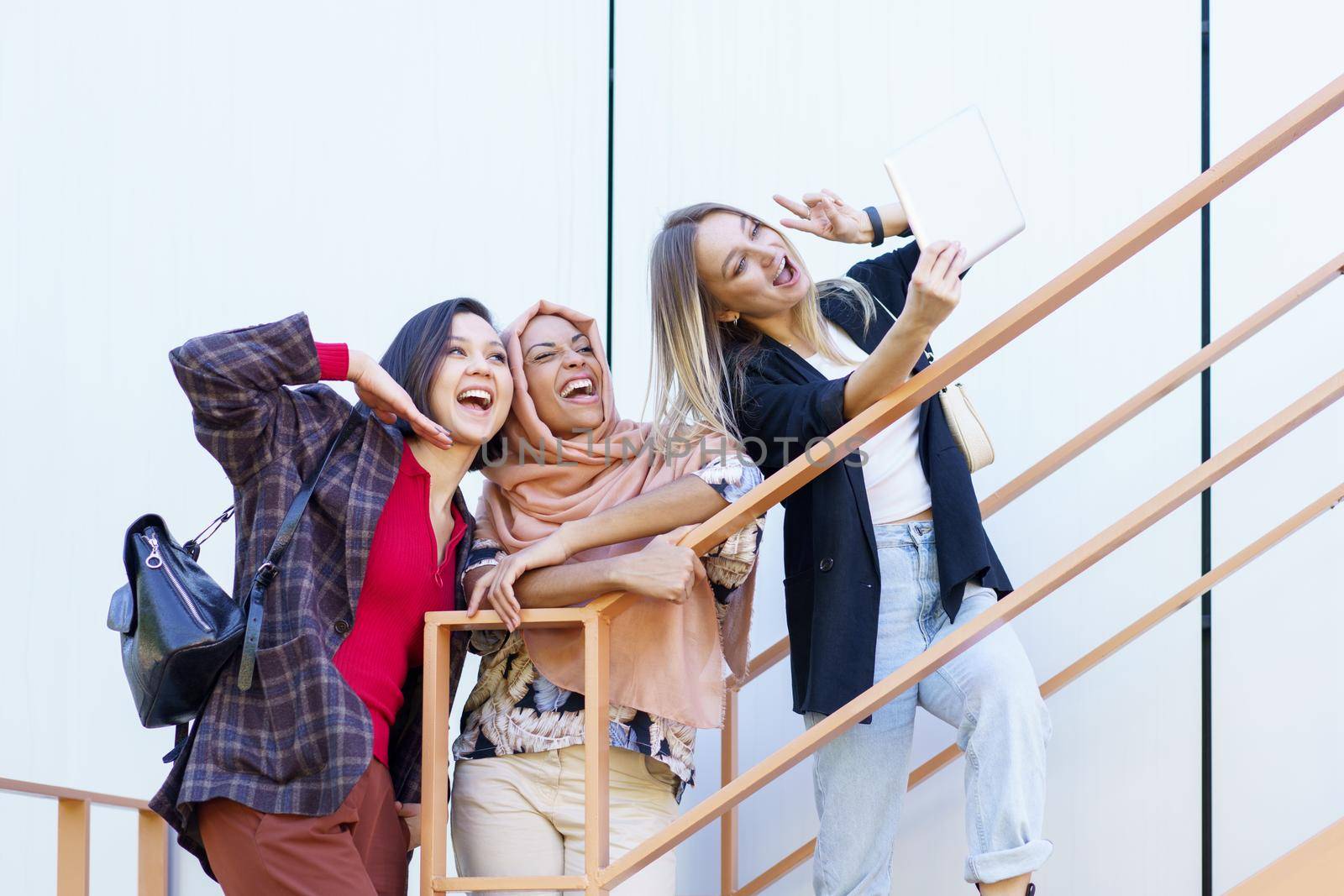 Excited young multiethnic female millennials smiling and taking selfie on tablet by javiindy
