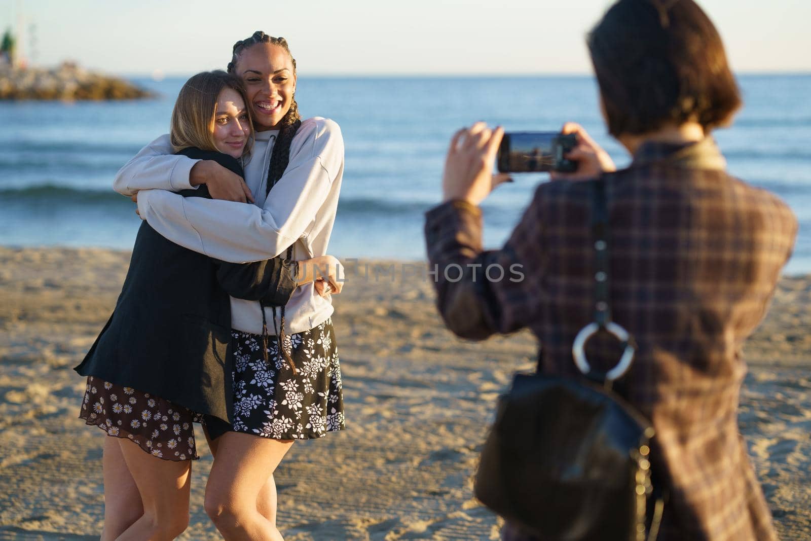 Faceless woman photographing positive diverse female friends on beach by javiindy