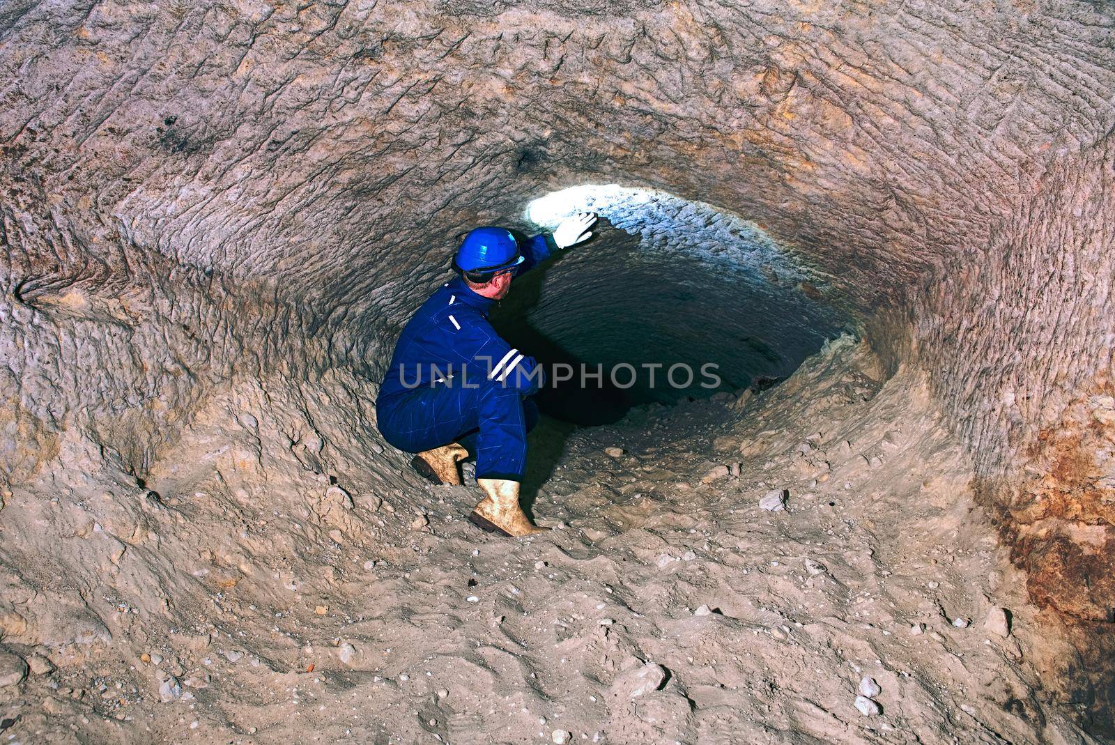 Staff do job in natural underground dome. Man with the illuminated headlight looks into the dark tunnel.