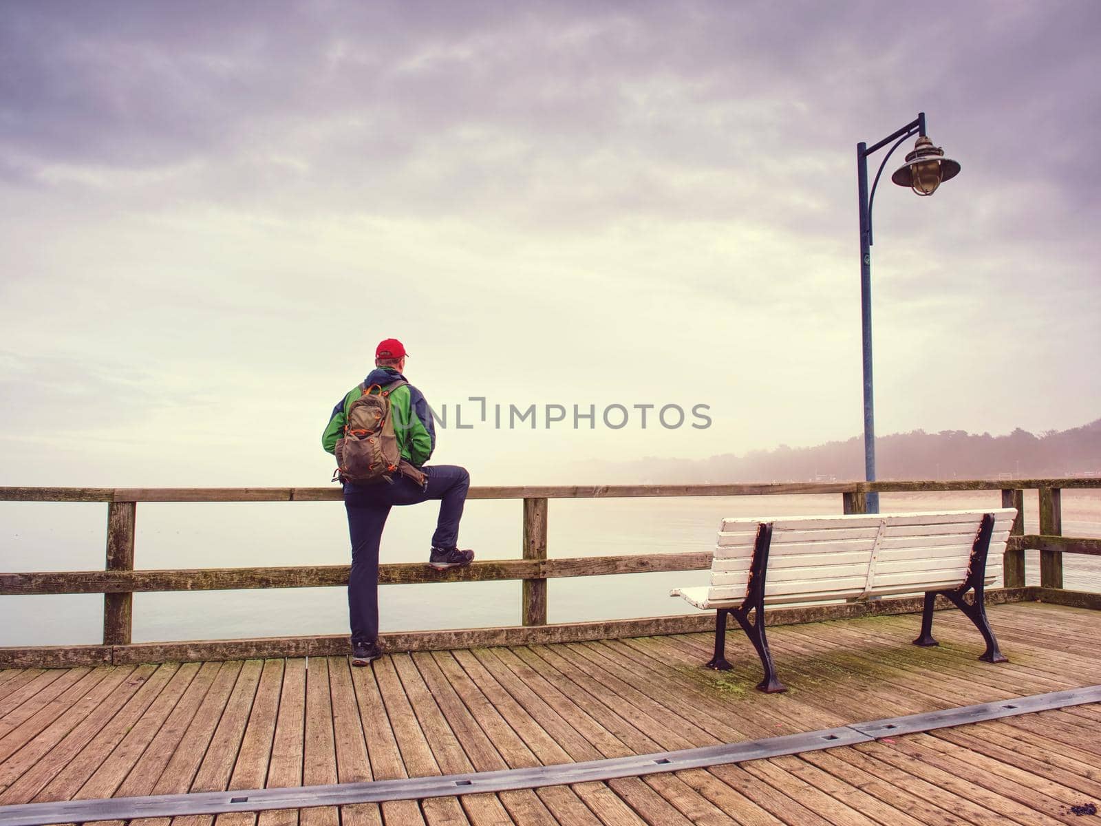 Thinking man on wooden pier on the background of sea hidden in mist.