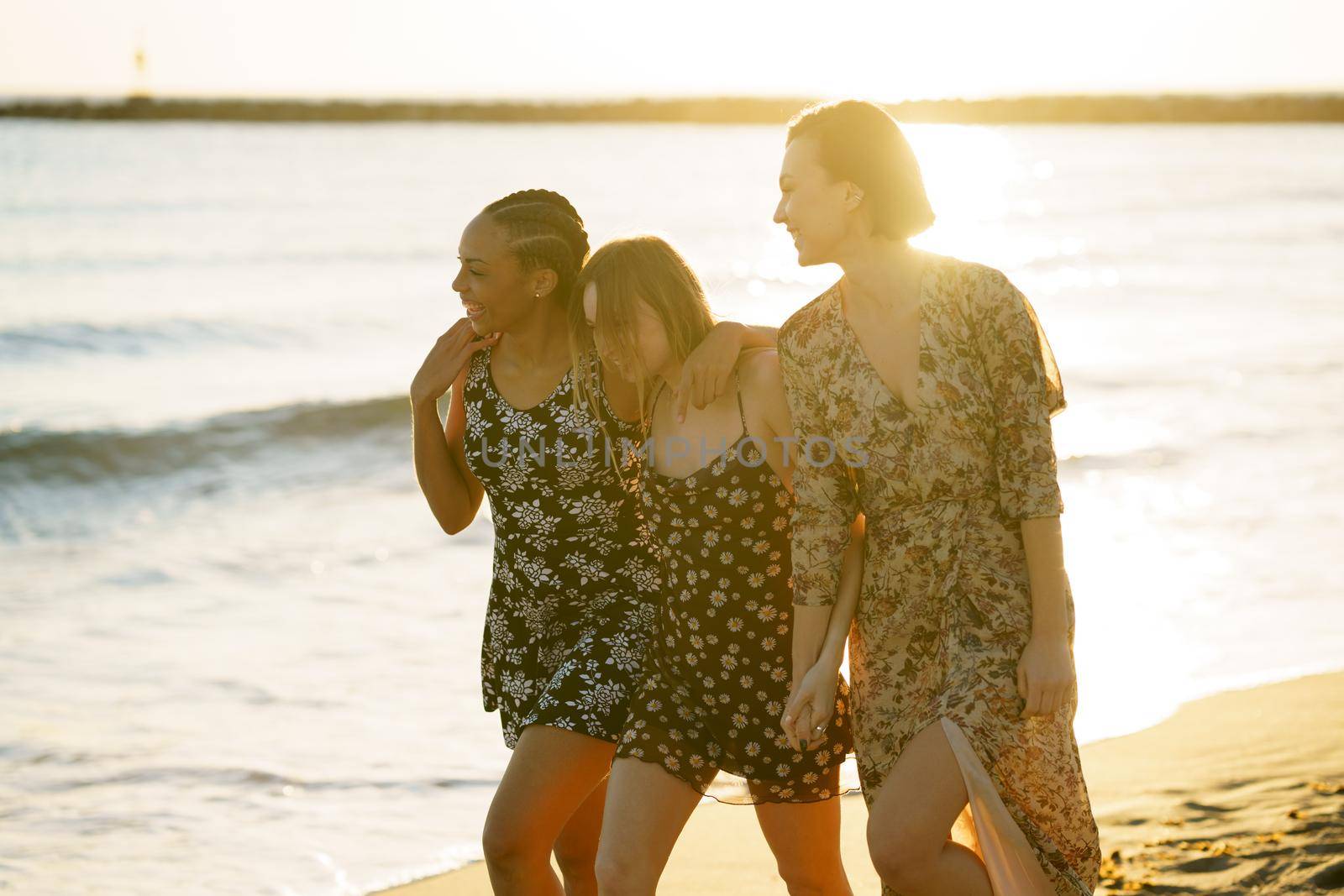 Delighted multiracial girlfriends walking on seashore by javiindy
