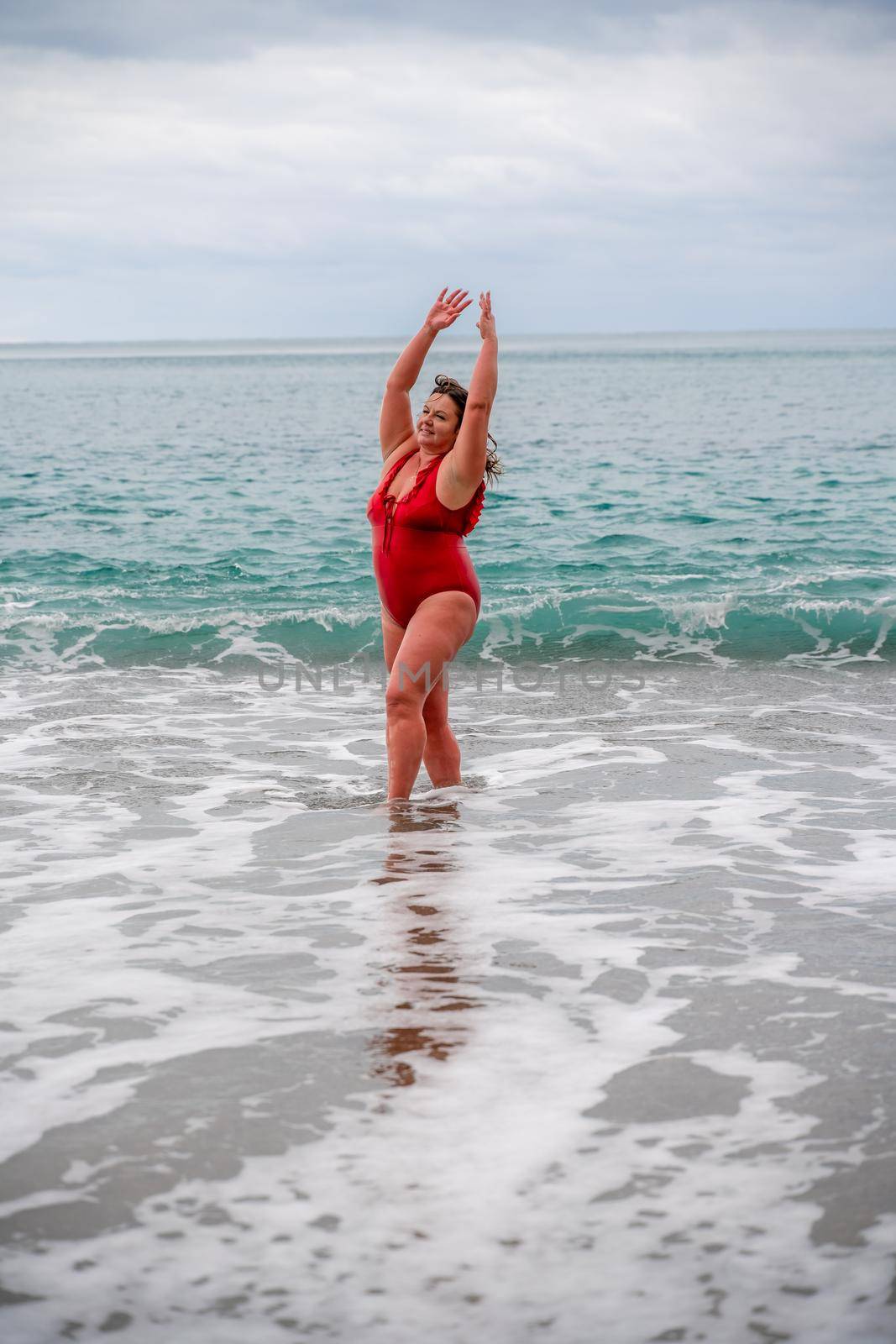 Woman in a bathing suit at the sea. A fat young woman in a red swimsuit enters the water during the surf.
