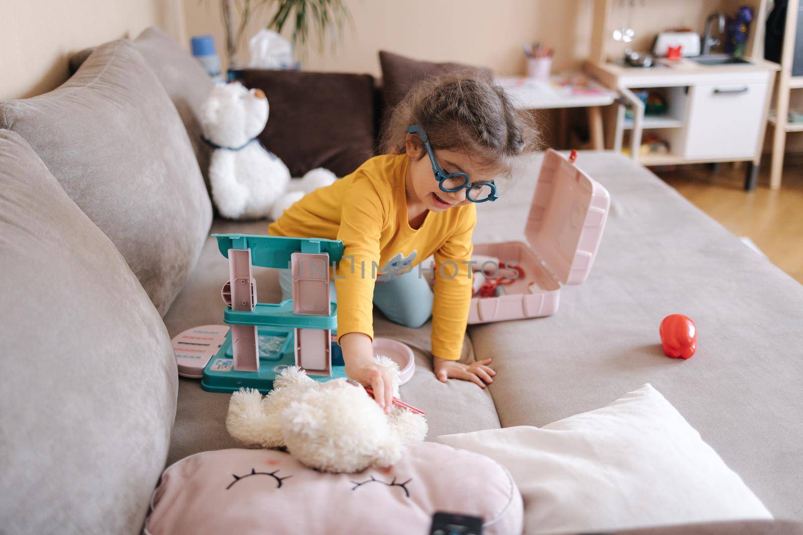 Adorable little girl playing doctor in her room. Cute three year old girl spend time playing. Girls wearing glasses yellow blouse and blue leggings. Ukrainian cute kid.