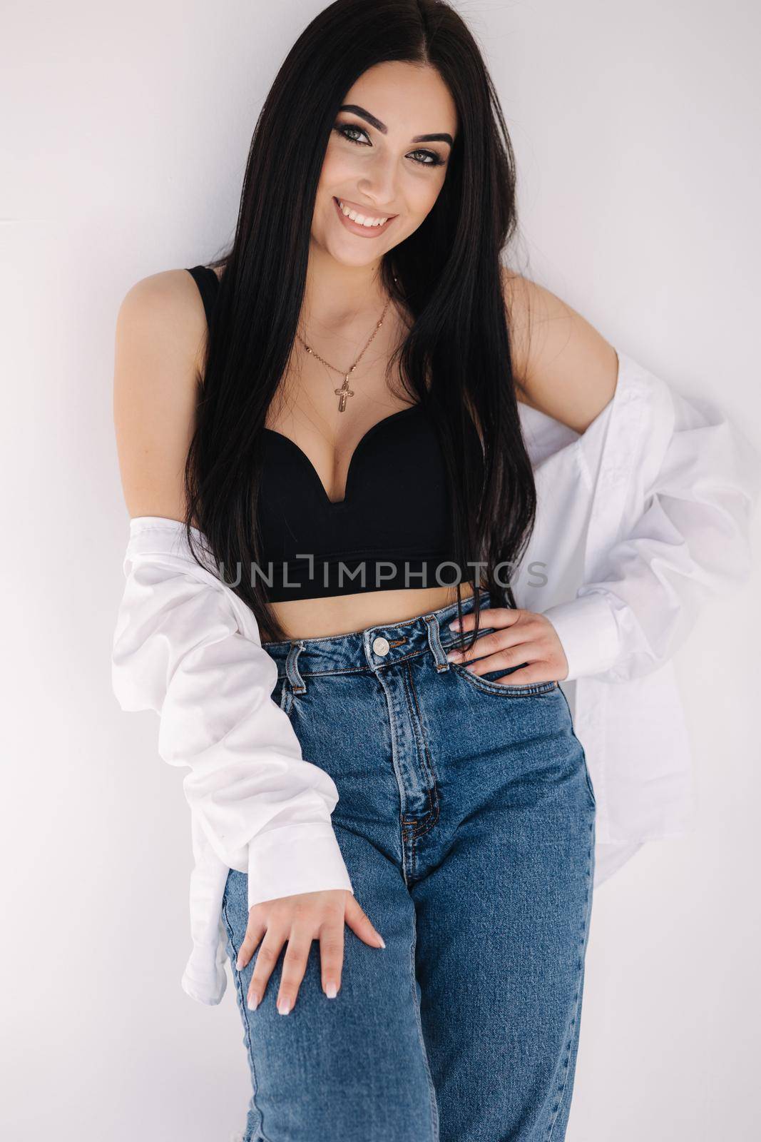 Pretty woman barefoot in studio. Beautiful brunette girl in black topic tiwh white shirt and blue denim jeans. White background of cyclorama.