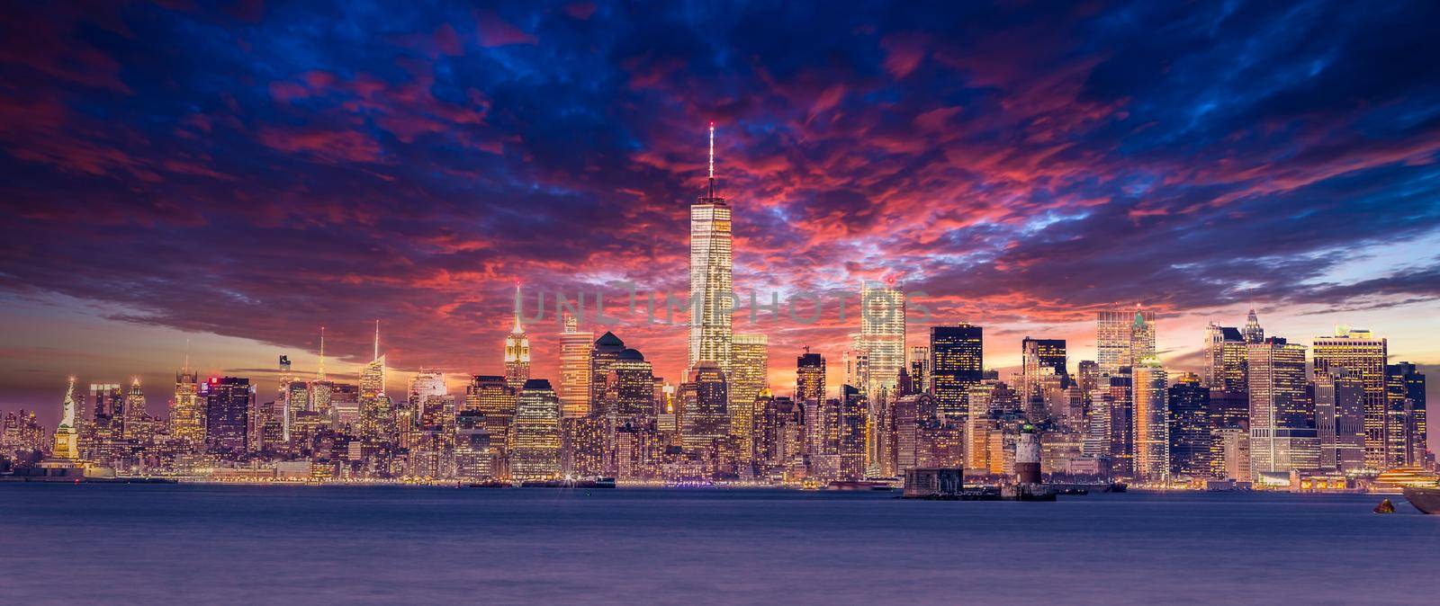 New York City Manhattan downtown skyline at dusk with skyscrapers illuminated over Hudson River panorama. Dramatic sunset sky. by kasto