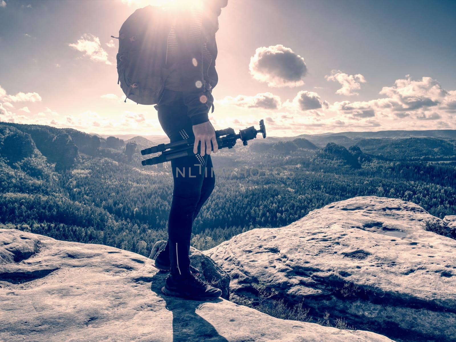 Man creator and photographer is setting up tripod for standing on rocky cliff.