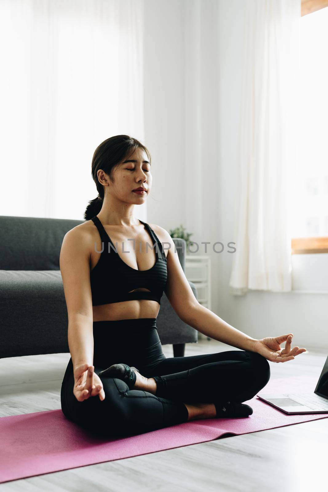 Young happy beautiful woman practicing yoga at home sitting in lotus pose on yoga mat meditating smiling relaxed. Mindfulness meditation concept.