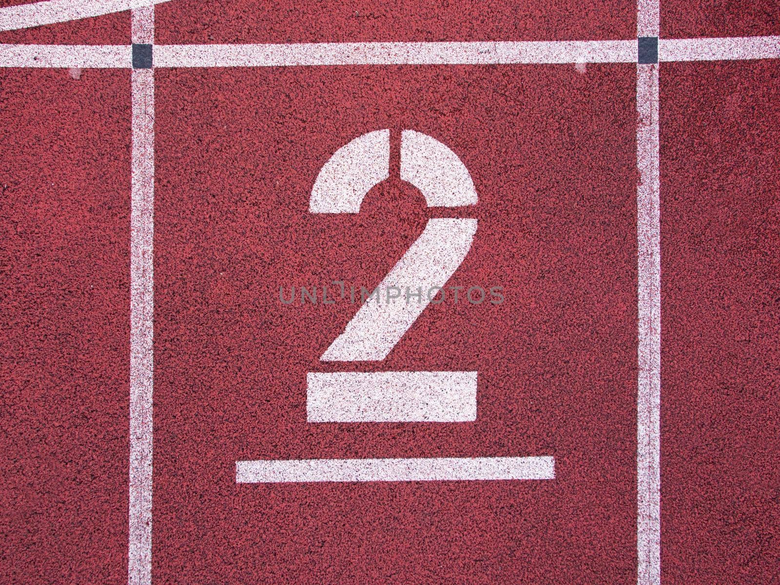 Number two. Big white track number on red rubber racetrack. Gentle textured running racetracks in small outdoor stadium.