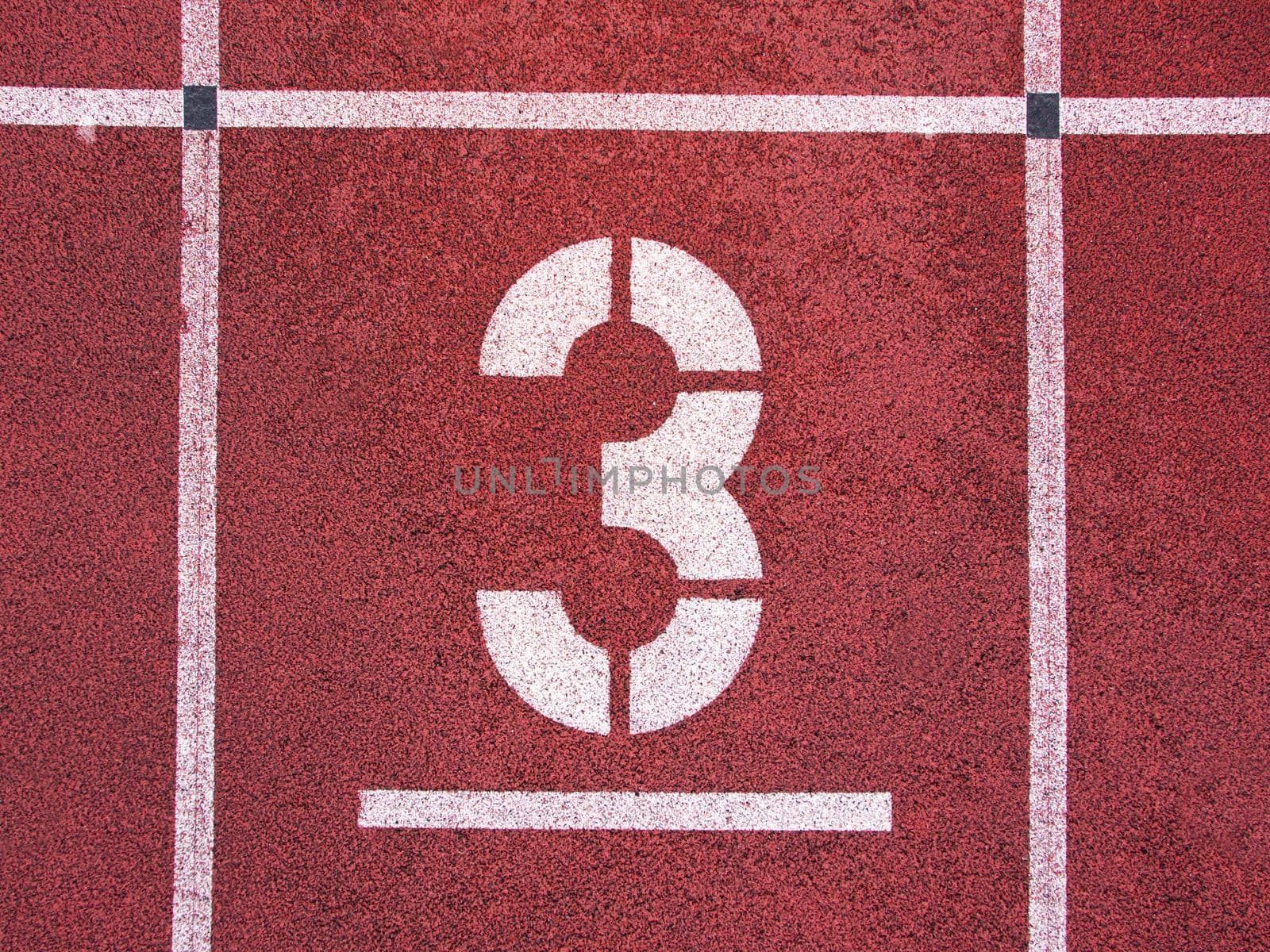 Number three. White track number on red rubber racetrack, texture of running racetracks in small stadium