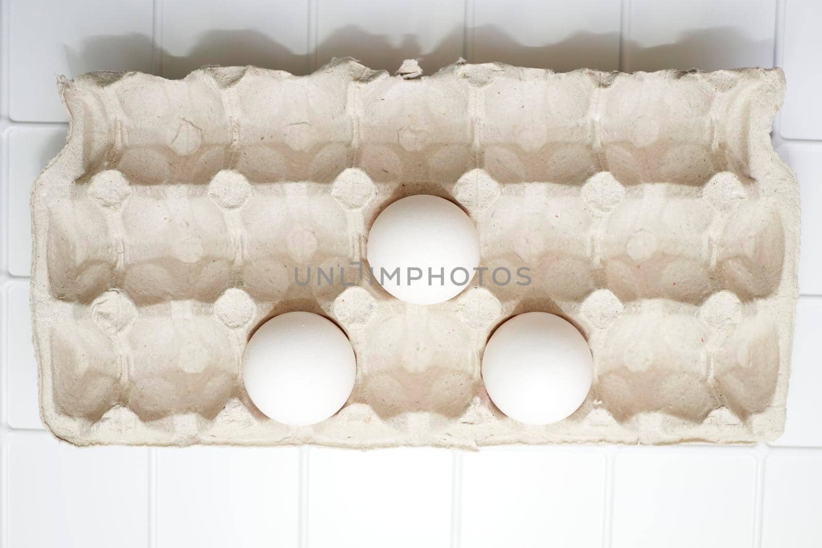 Three white eggs in a cardboard tray on a white background by jovani68