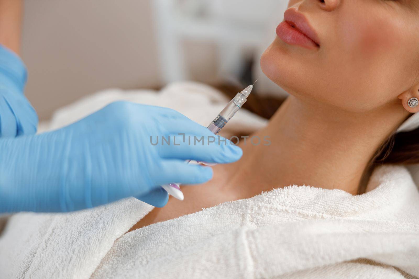 Closeup of young woman getting hyaluronic acid injections in chin at beauty salon. Cosmetology